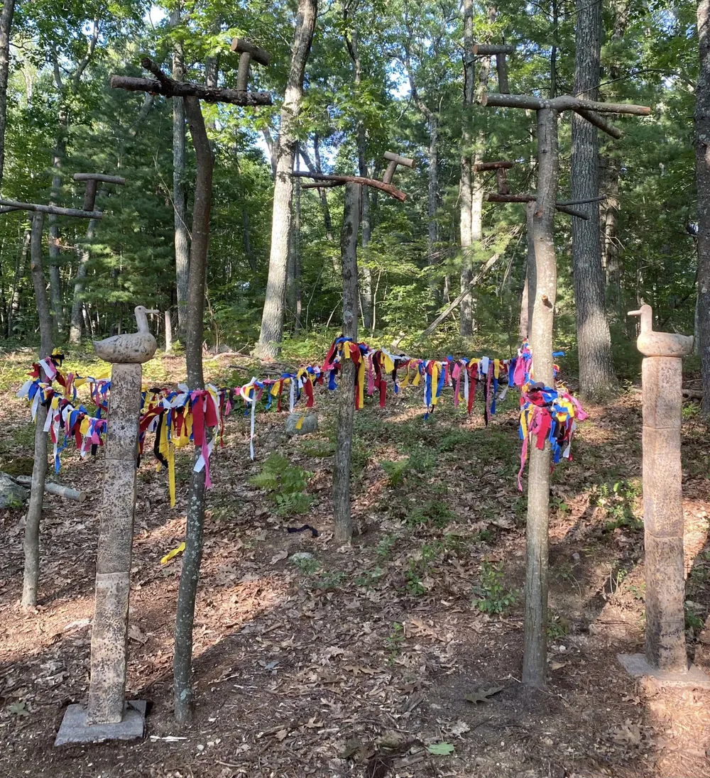 Sanctuary standing in the woods: a ring of tree-trunk posts with cross-arms, strung with a rice-straw rope hung with red, blue, yellow and white cloth strips, and two clay sotdae bird-poles at either side.