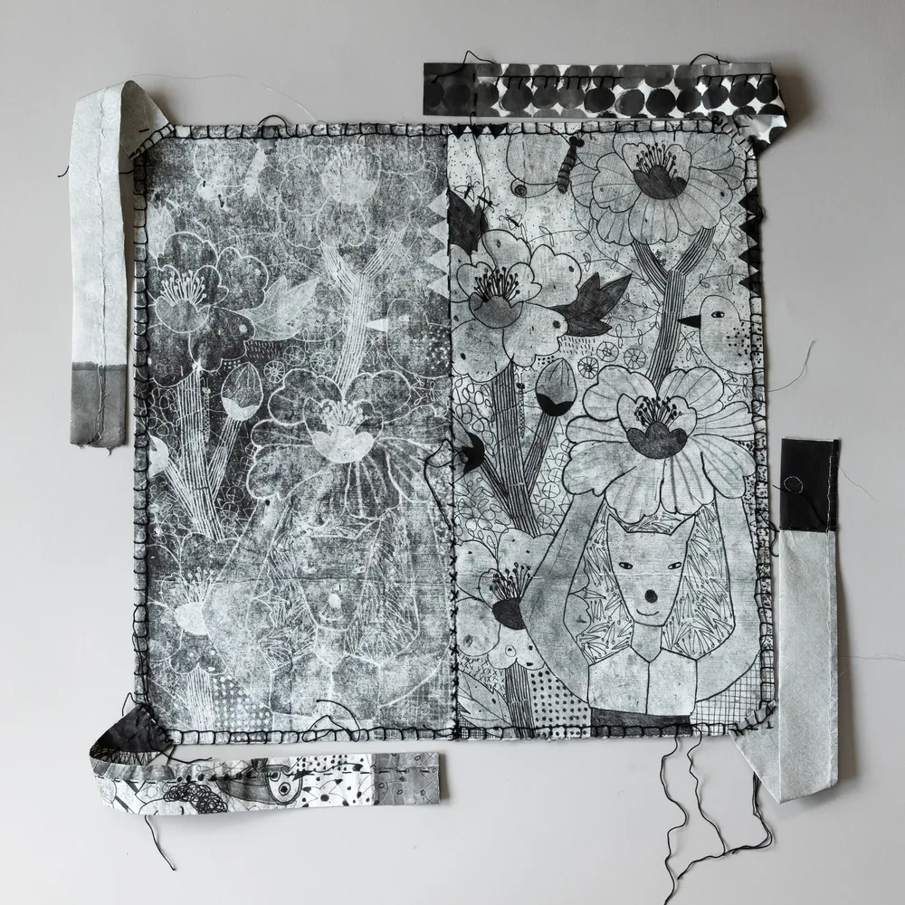 A square stitched hanji bojagi in black and white: ghostly printed flowers across the left half, a finely drawn fox-faced figure under a large flower on the right, a dotted strip along the top and paper straps at the edges.