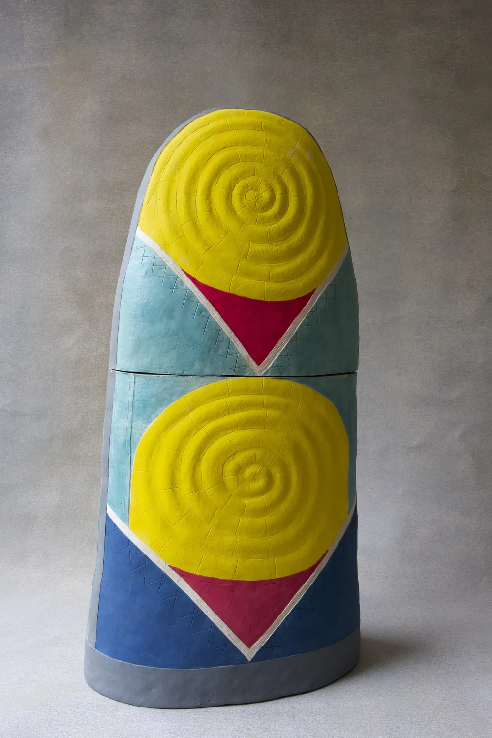 Thimble 1: two large clay thimble forms stacked on the photographer’s grey ground — a yellow spiral cap over pale teal with a magenta V, sitting on a second yellow spiral over blue with a grey foot band.