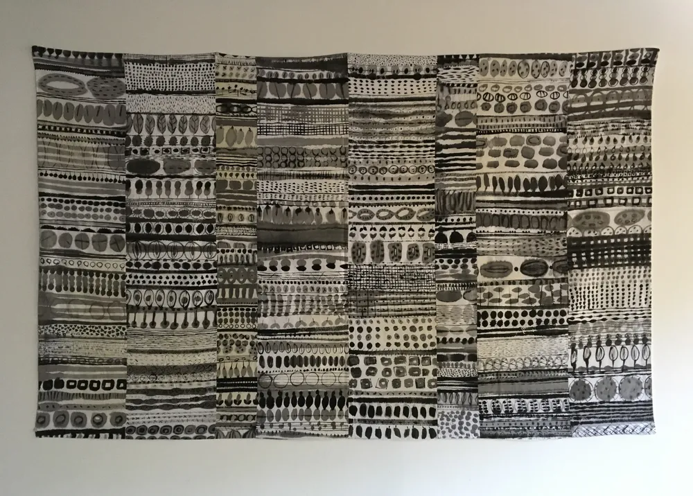 Each Seed a New Life, a wide horizontal bojagi pieced from eight linen napkin strips, each brushed in sumi ink with rows of ovals, seeds and pods in black and grey.