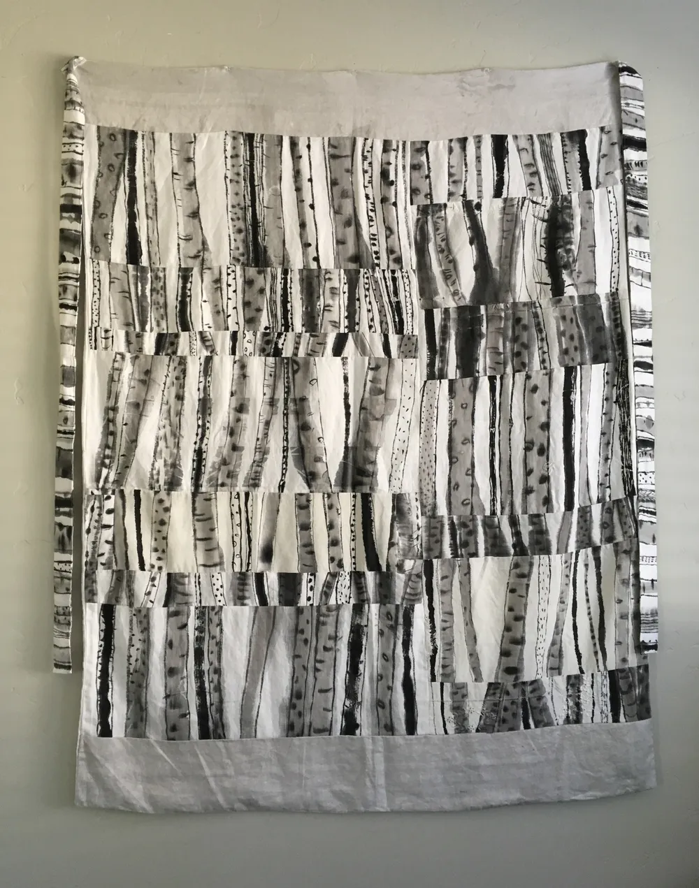 Birch, a patchwork cloth bojagi of sumi-ink birch-bark stripes on used linen, hung on a wall with pale bands top and bottom and narrow drawn strips falling at either side.