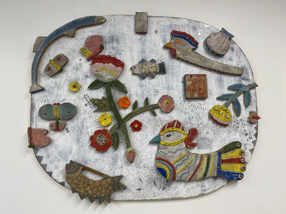 The largest of the talisman panels — a big irregular oval on a densely drawn white and grey ground, covered with ceramic pieces: a carp, a rooster, a red peony, butterflies, small birds and a red 福 (fortune) seal tile.