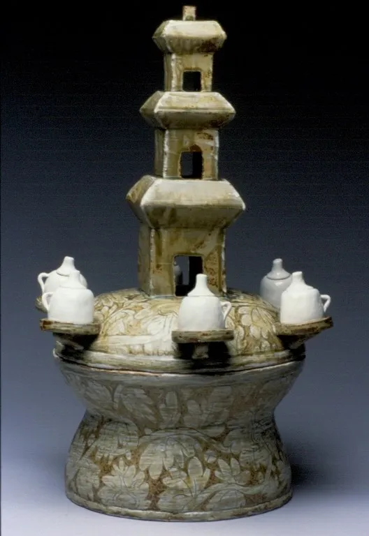 A celadon three-tier pagoda censer with six small white teapots ringing an incised lotus lid, standing on a wide footed base.