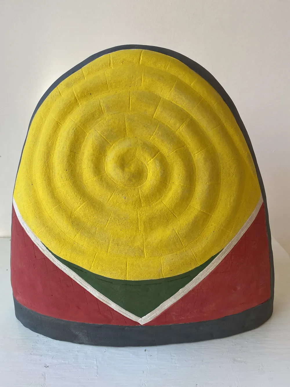 Thimble 2, a large clay thimble dome with a yellow concentric spiral filling its face, a red body, a green and white chevron and a dark rim.
